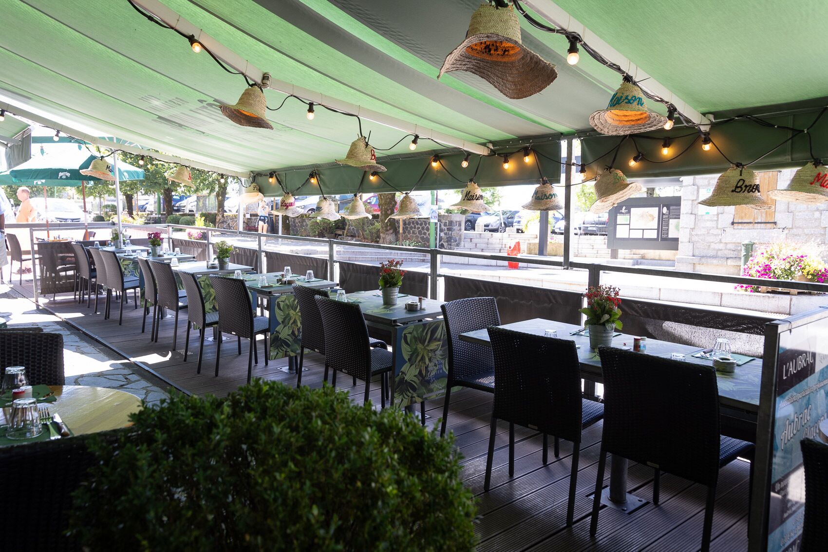 An outdoor dining area with tables and chairs, string lights, and hanging hats.
