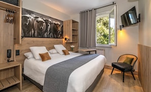 A bedroom with a large bed, a TV, a window with curtains, a desk, and a chair.