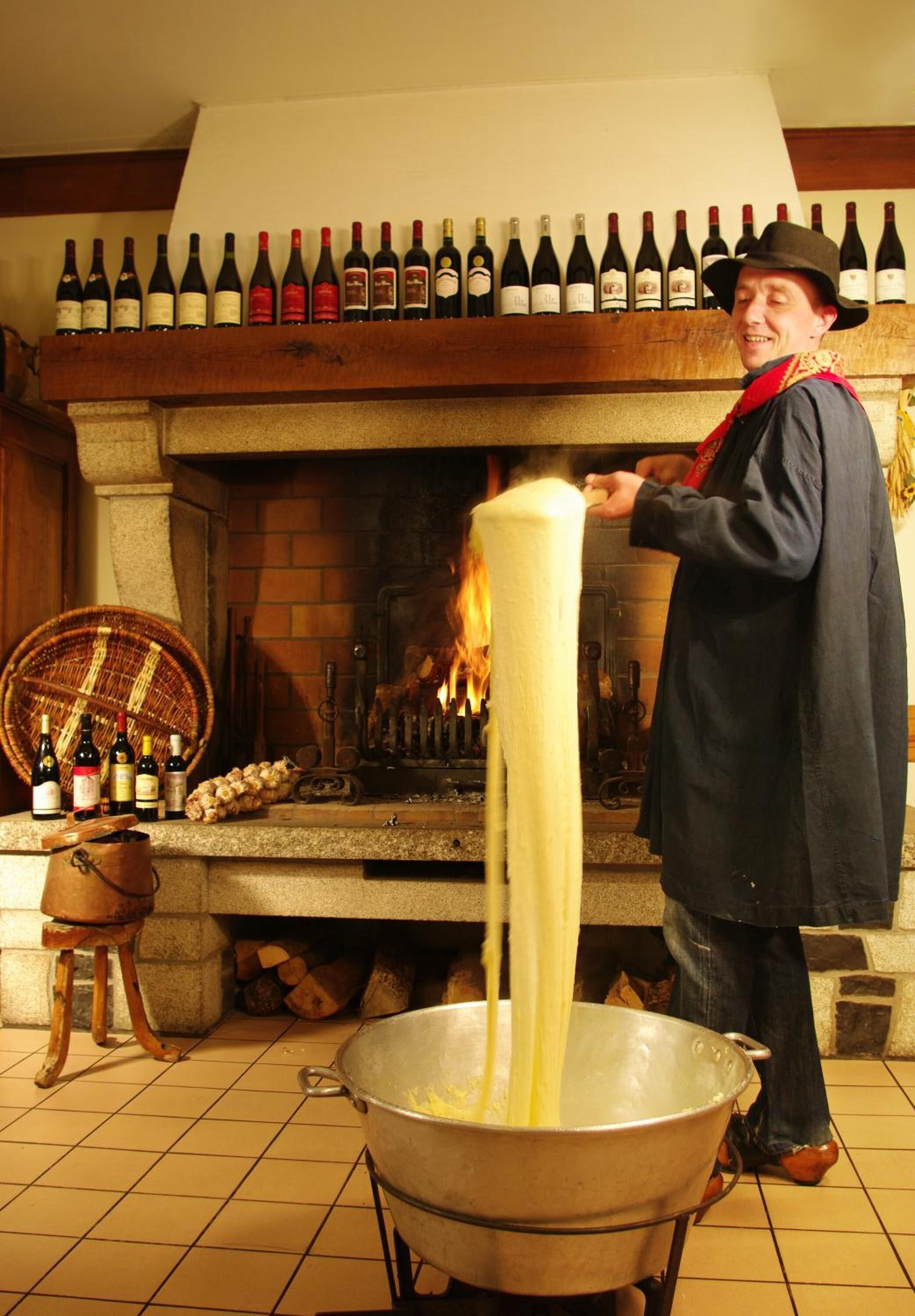 A chef cooking spaghetti in a large pot in a kitchen with a wine rack above the stove.