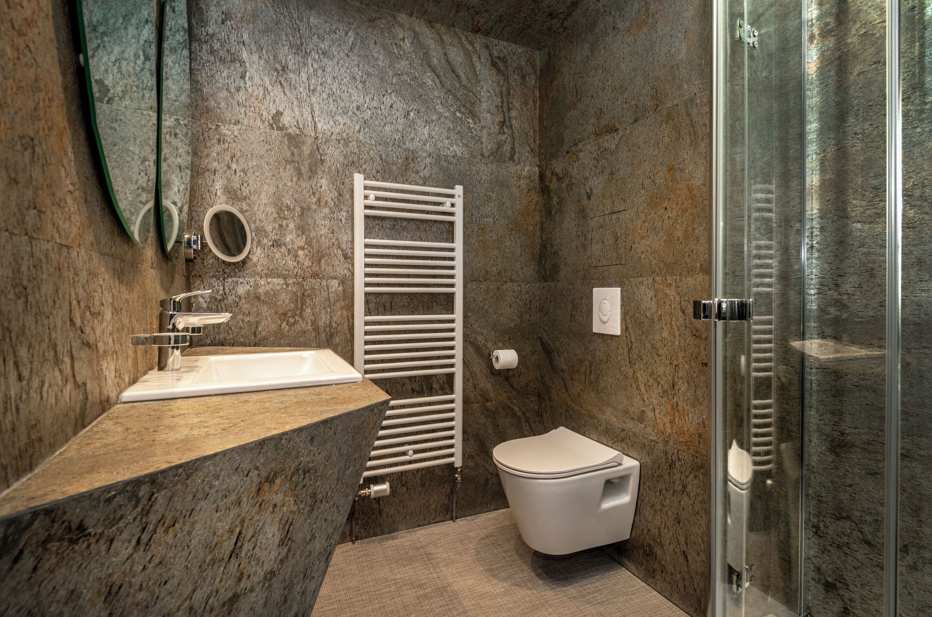 Un baño con lavamanos de mármol, inodoro, toallero y cabina de ducha con paredes de vidrio.