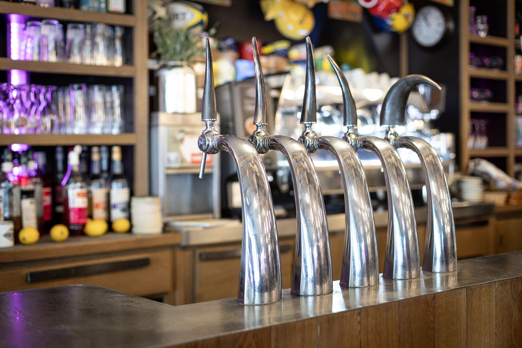 Un bar con múltiples grifos y estantes llenos de botellas al fondo.