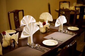 A dining table set with white napkins, silverware, and a vase with a red rose. - Five Elements Hotels North Avenue Delhi (New Delhi)