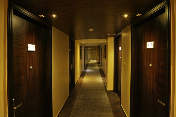 A hotel hallway with wooden doors, a carpeted floor, and a light fixture on the ceiling.