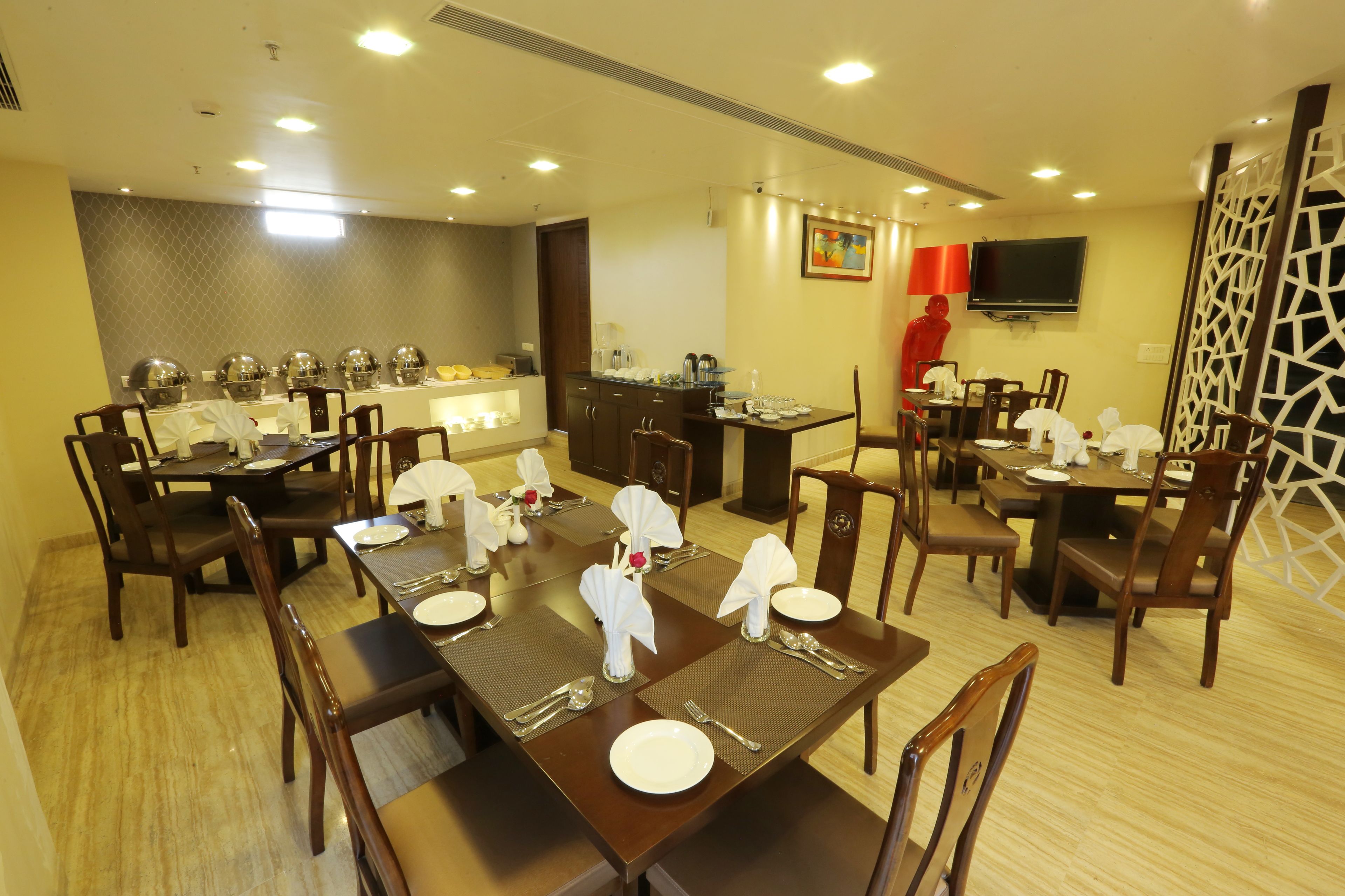Un espace repas avec plusieurs tables dressées pour les invités, un coin cuisine et un téléviseur fixé au mur.