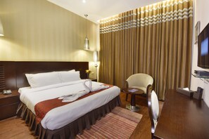 A hotel room with a large bed, a bedside table with a lamp, a chair, a TV, and a curtain. - Five Elements Hotels North Avenue Delhi (New Delhi)