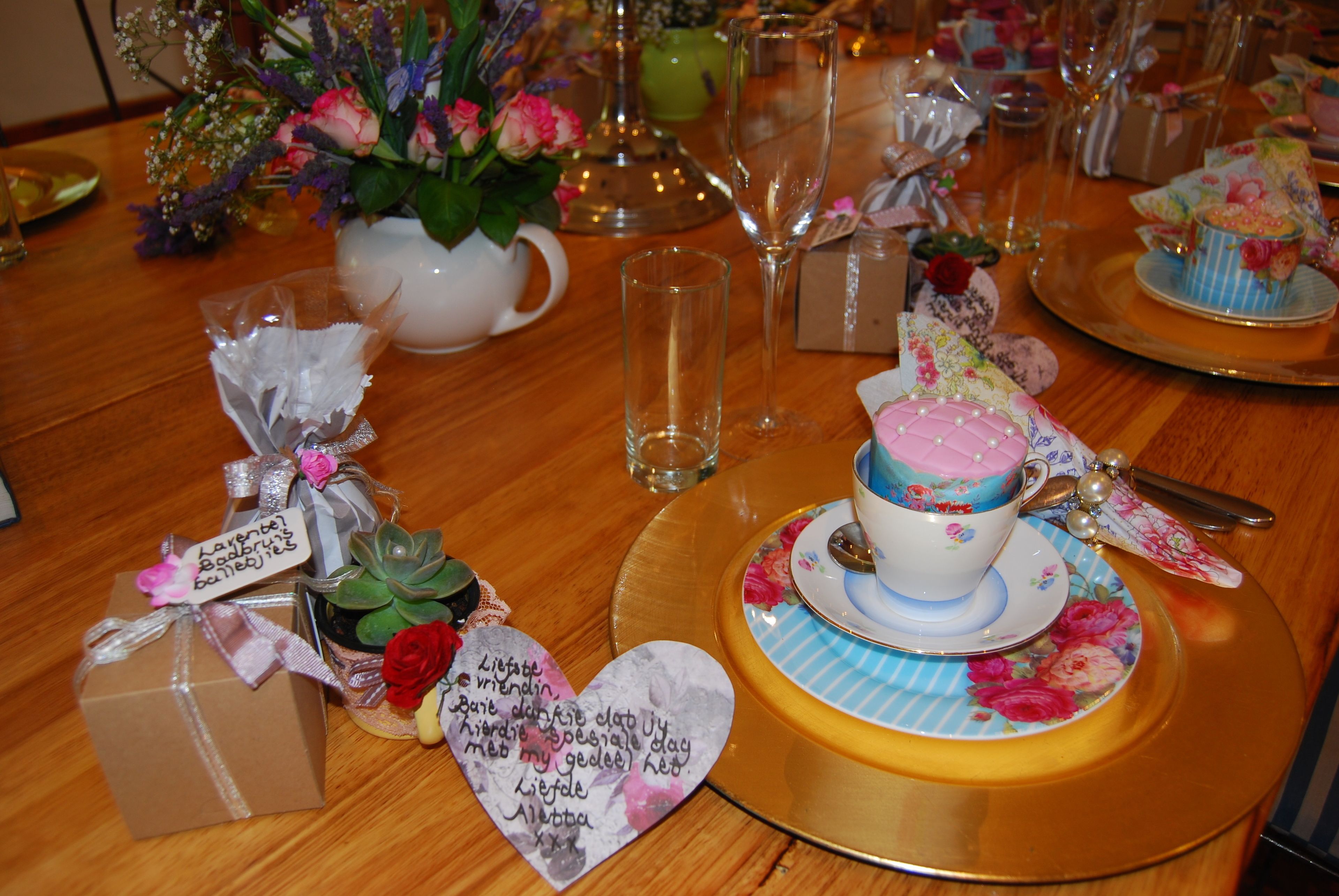 A table set with a floral-patterned cup, a small gift box, and a decorative heart-shaped note.