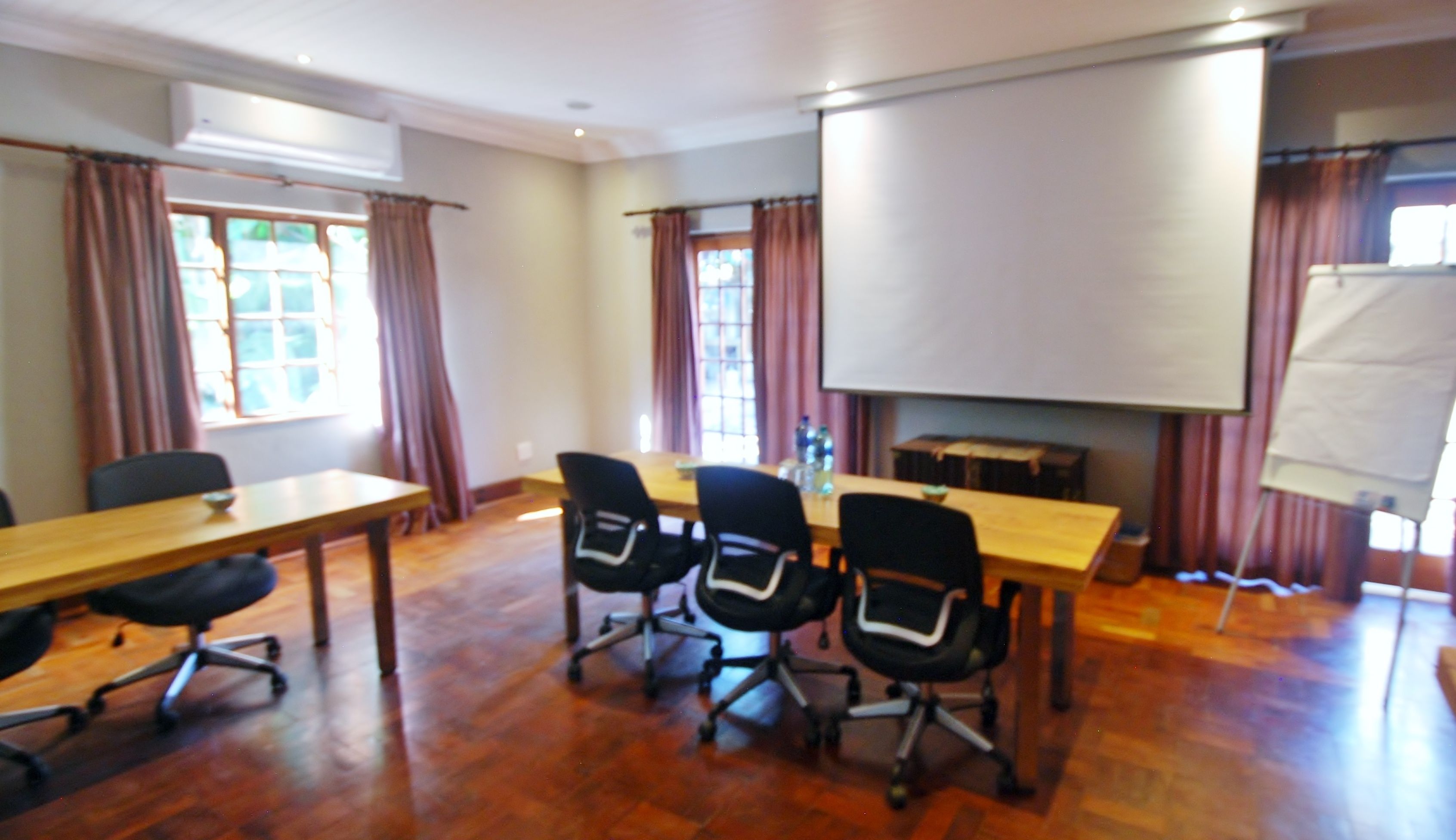 A conference room with a wooden table, four office chairs, a projector screen, and a whiteboard.