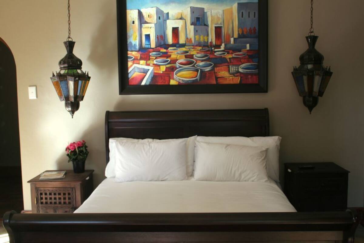 Ein Schlafzimmer mit einem großen Bett, zwei Wandlampen, einem Gemälde über dem Bett und einem kleinen Tisch mit einer Blumenvase.
