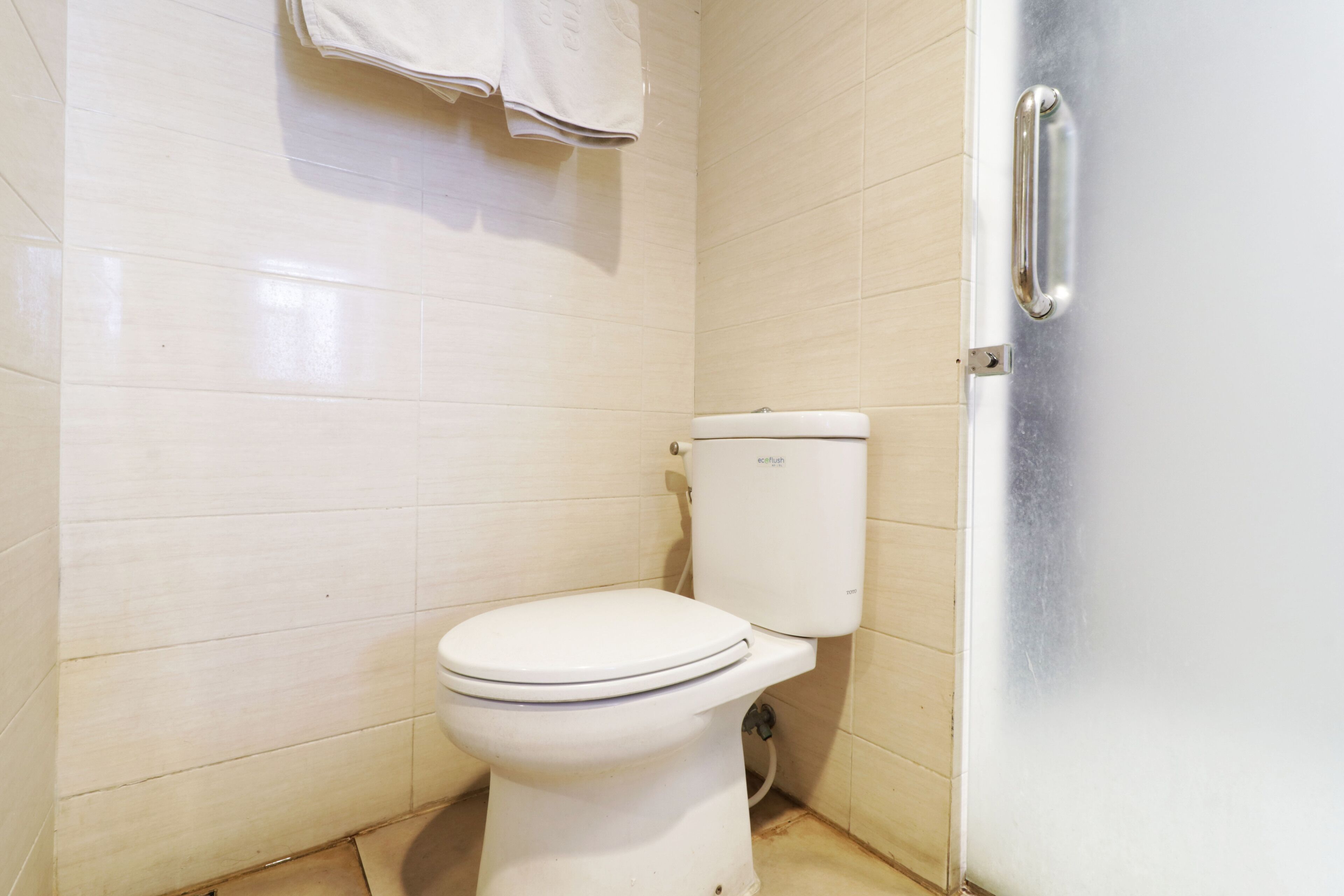 A small, clean bathroom with a white toilet, a towel hanging on the wall, and a door with a handle.
