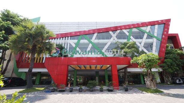 A modern building with a distinctive red and white facade, featuring a large entrance with a covered walkway and potted plants. - Dewarna Hotel & Convention (Bojonegoro)