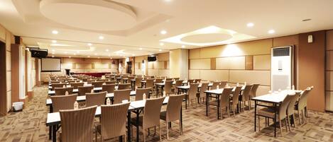 A conference room with rows of tables and chairs, equipped with projectors and a large screen.