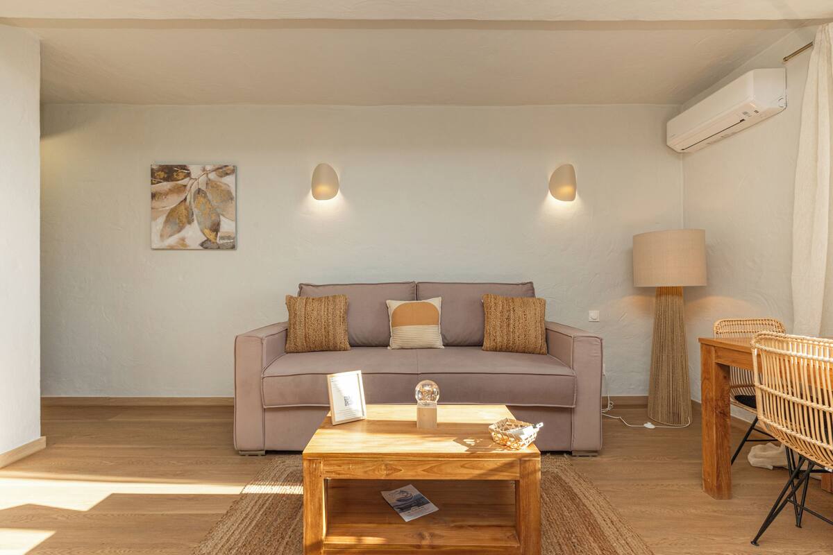 A living room with a sofa, a coffee table, a lamp, and a wall-mounted air conditioner.