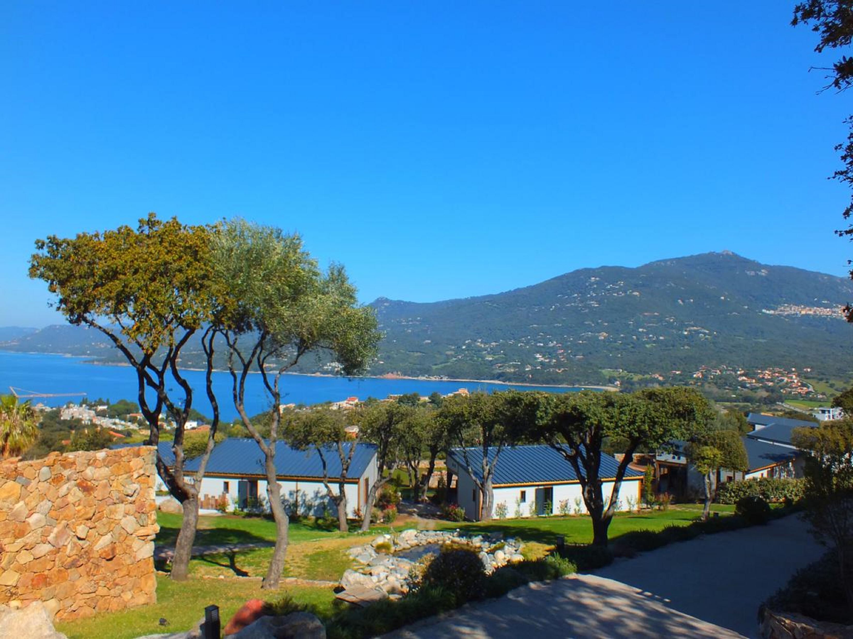 A coastal property with stone walls, a stone pathway, and a view of the sea and a mountain.