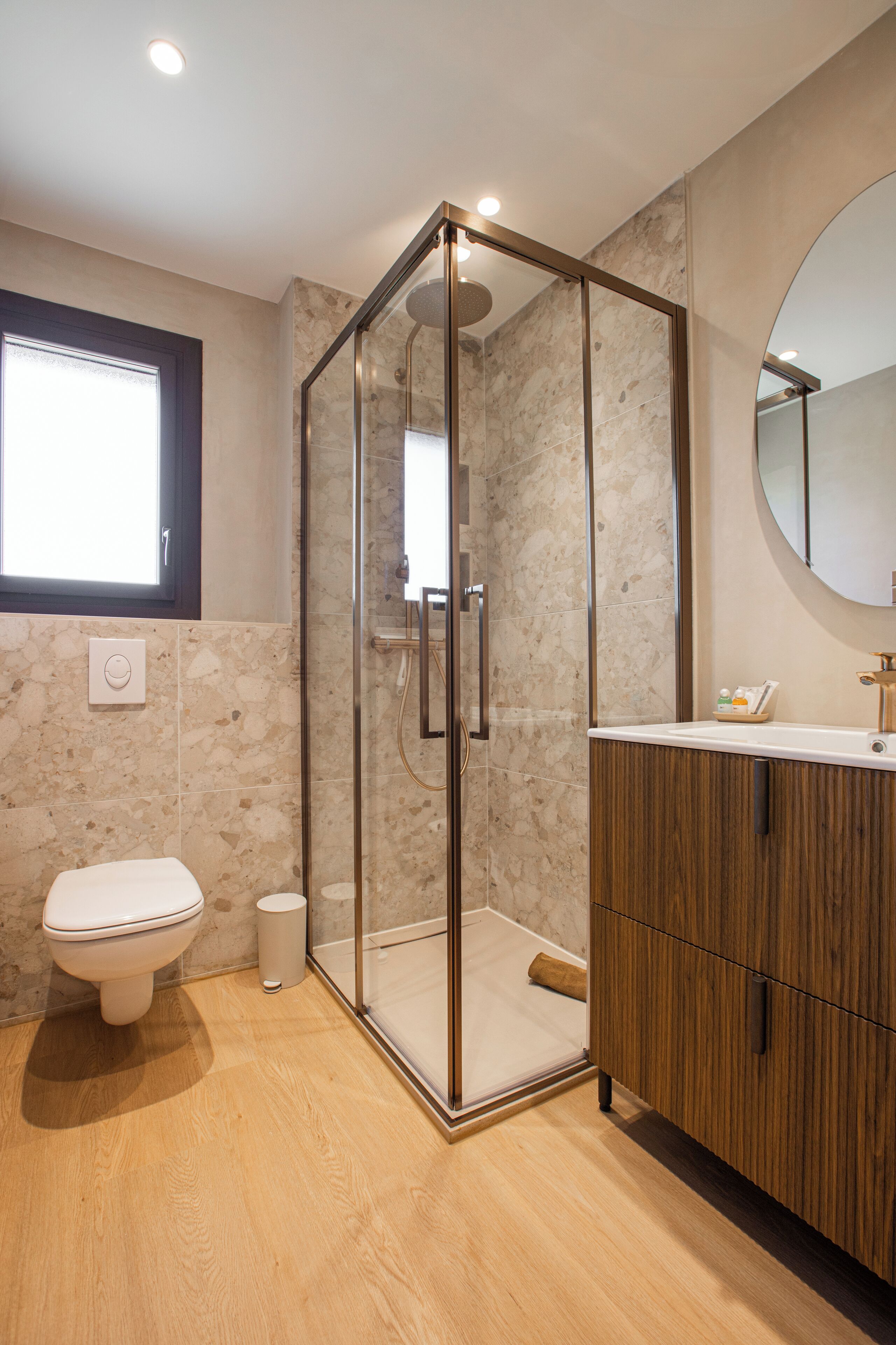 A modern bathroom with a glass-enclosed shower, a toilet, and a wooden vanity with a mirror.