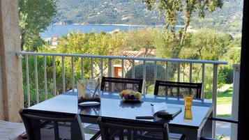 A balcony with a table set for two, overlooking a scenic view of a lake and hills.