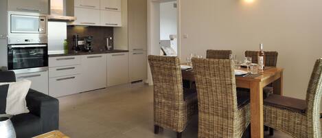 A modern kitchen with built-in appliances, a dining area with wicker chairs, and a small seating area with a table and cushions.