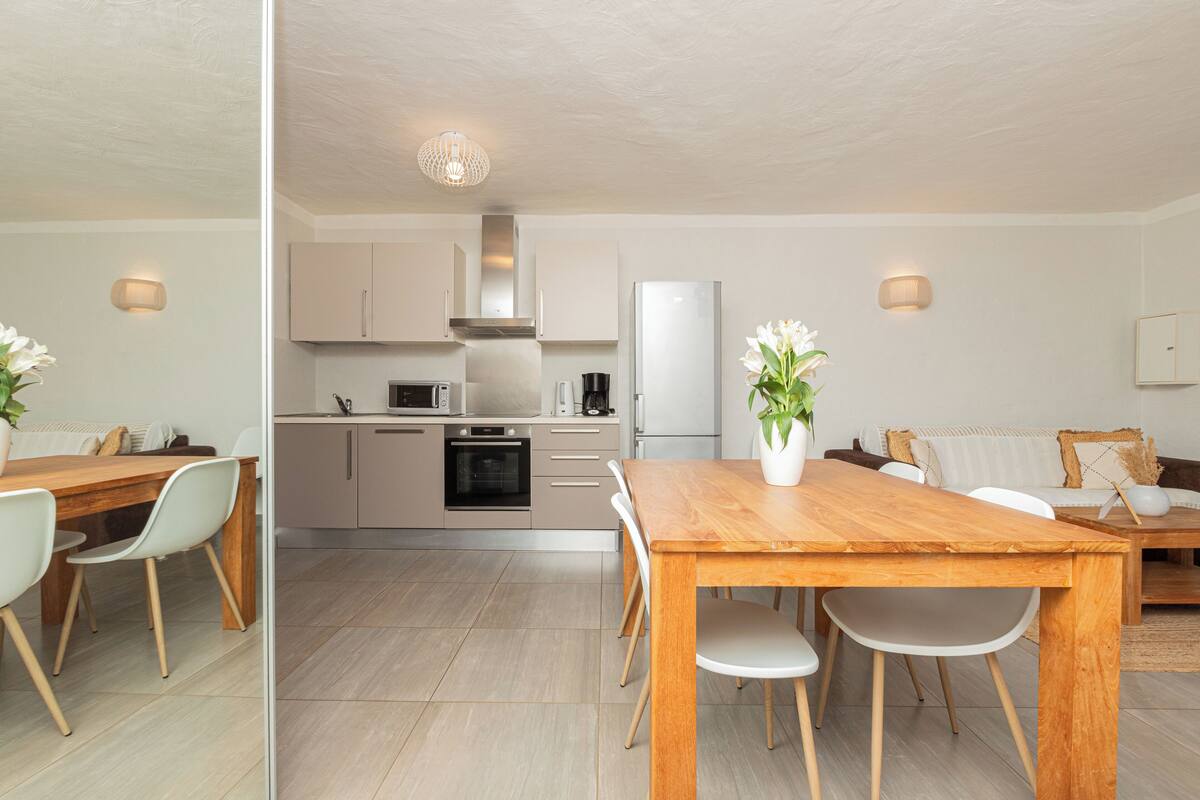 A modern kitchen with a dining area, featuring a wooden table and chairs, a refrigerator, and a microwave.