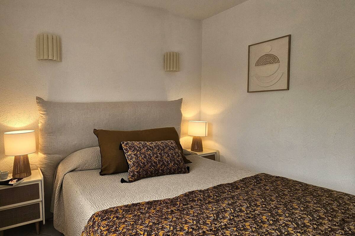 A bedroom with a bed, two bedside lamps, a nightstand, a wall-mounted radiator, and a framed picture.