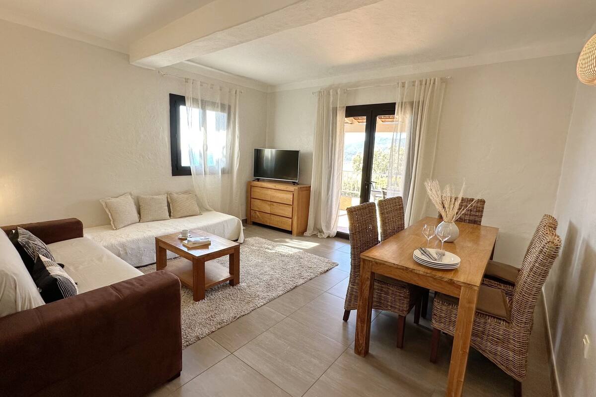 A modern living room with a sofa, coffee table, TV, and dining area with chairs and a table set for two.