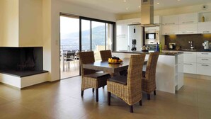 Une cuisine moderne avec des meubles blancs, un grand îlot central et un coin repas doté de chaises en osier.