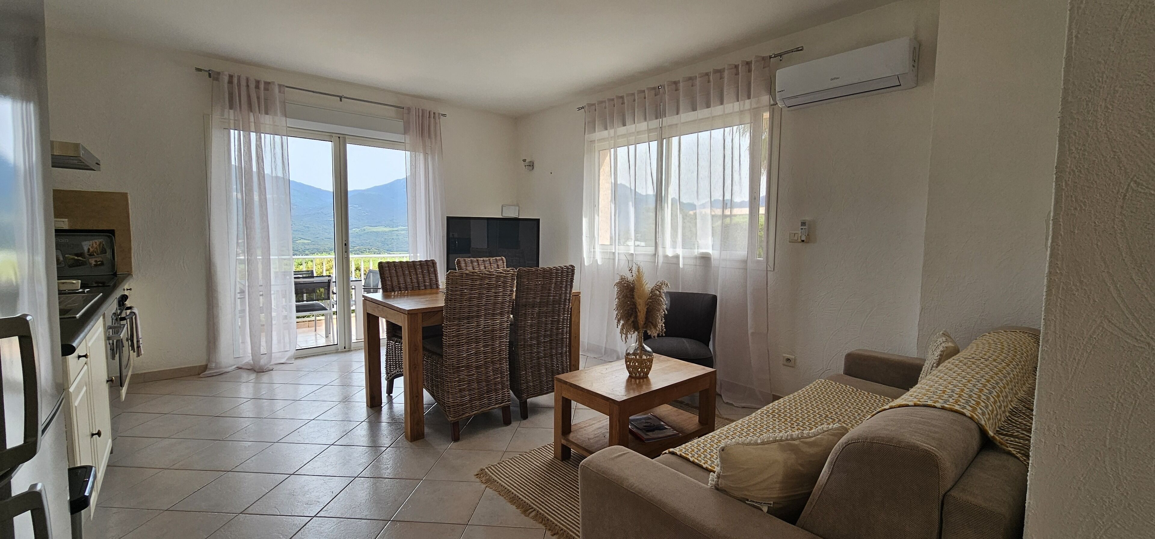A living room with a sofa, a table, and chairs, a television, and a view of mountains through large windows.