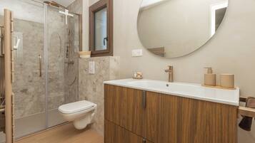 Een moderne badkamer met een glazen douchecabine, een houten wastafelmeubel en een ronde spiegel.