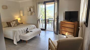 Een slaapkamer met een bed, een televisie, een houten dressoir en een balkon met uitzicht.