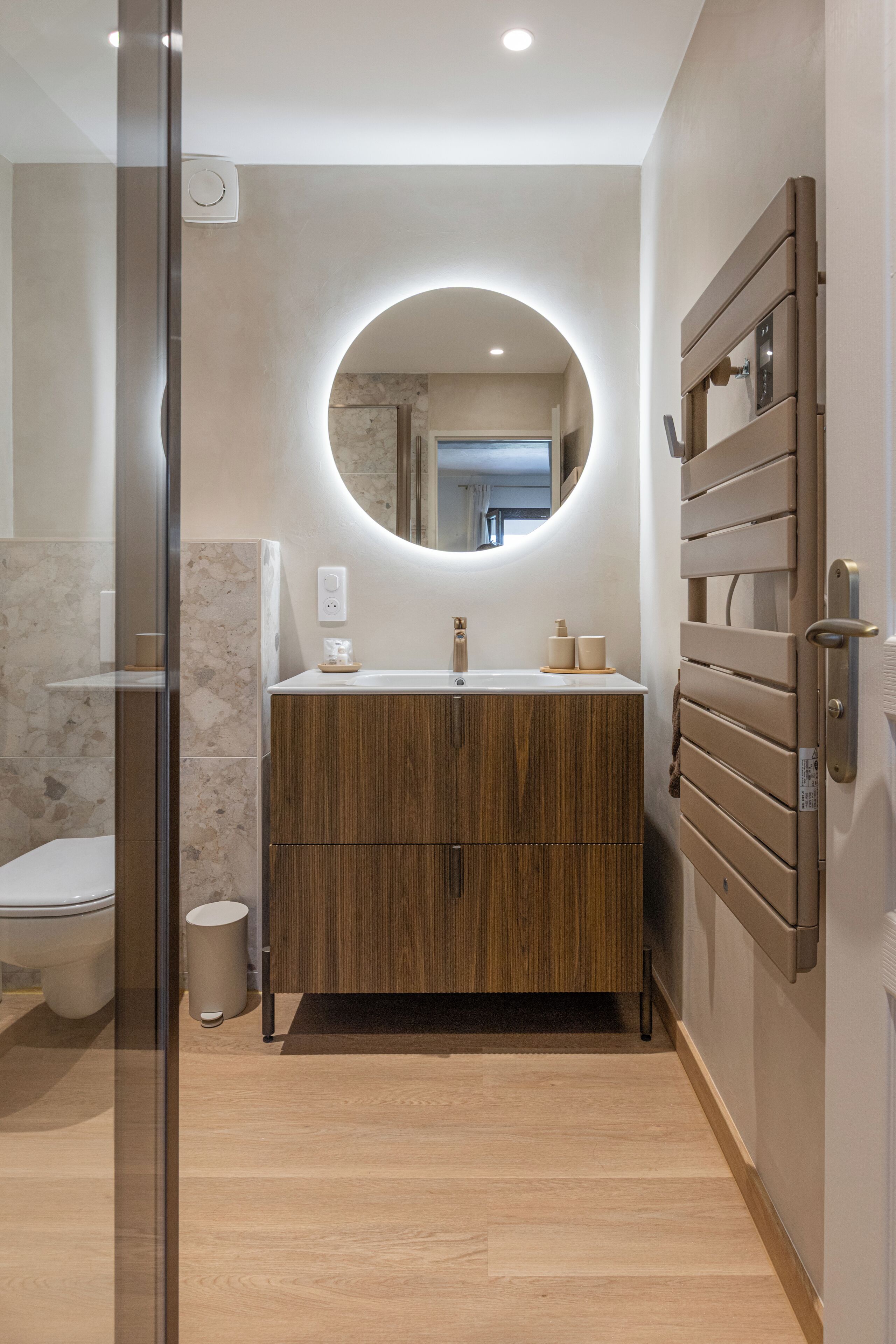 Ein modernes Badezimmer mit einem Holzlagerflansch, einem runden Spiegel und einer Toilette.