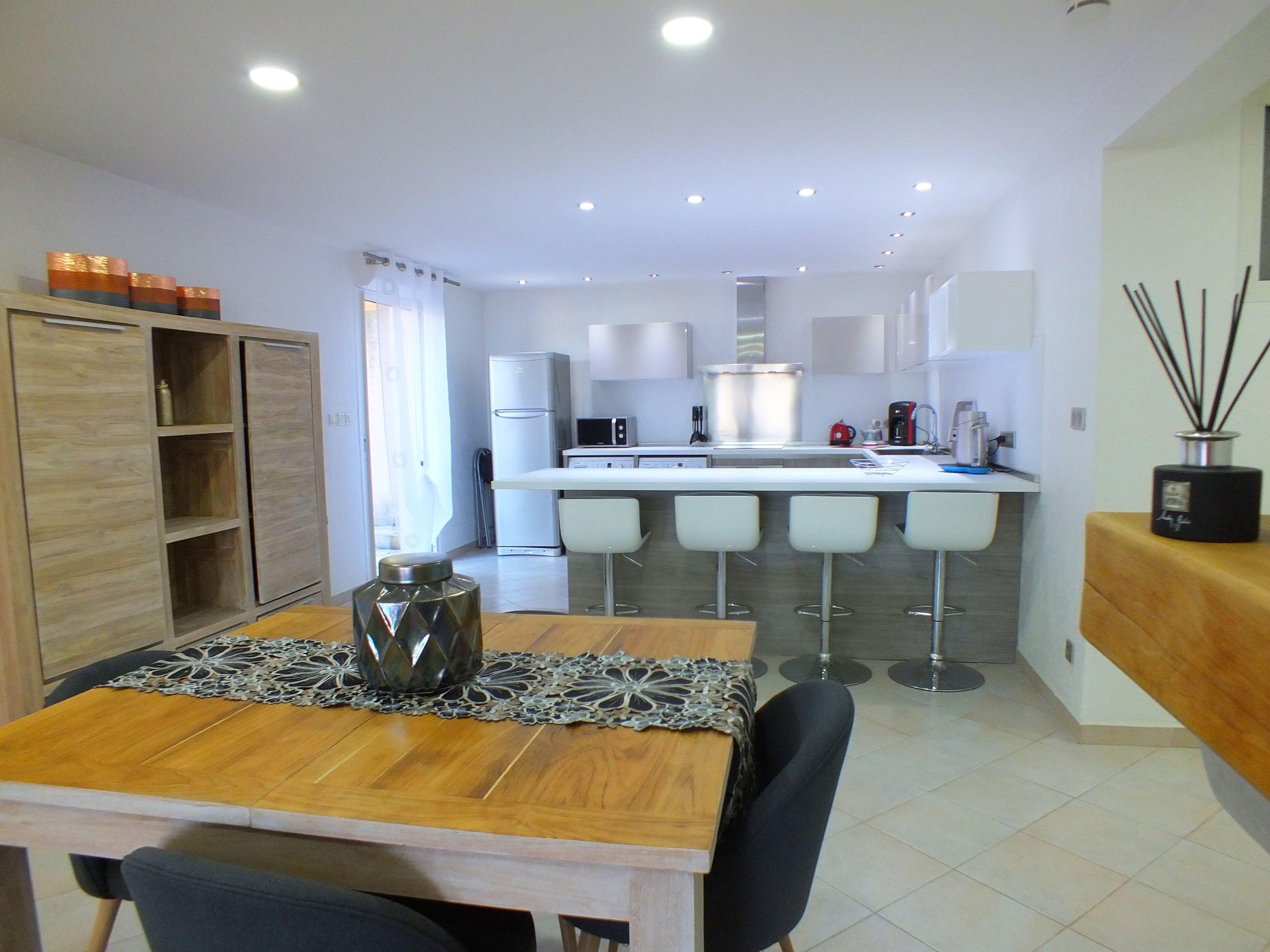 Une cuisine moderne avec des meubles blancs, un îlot central et un coin repas comprenant une table et des chaises en bois.