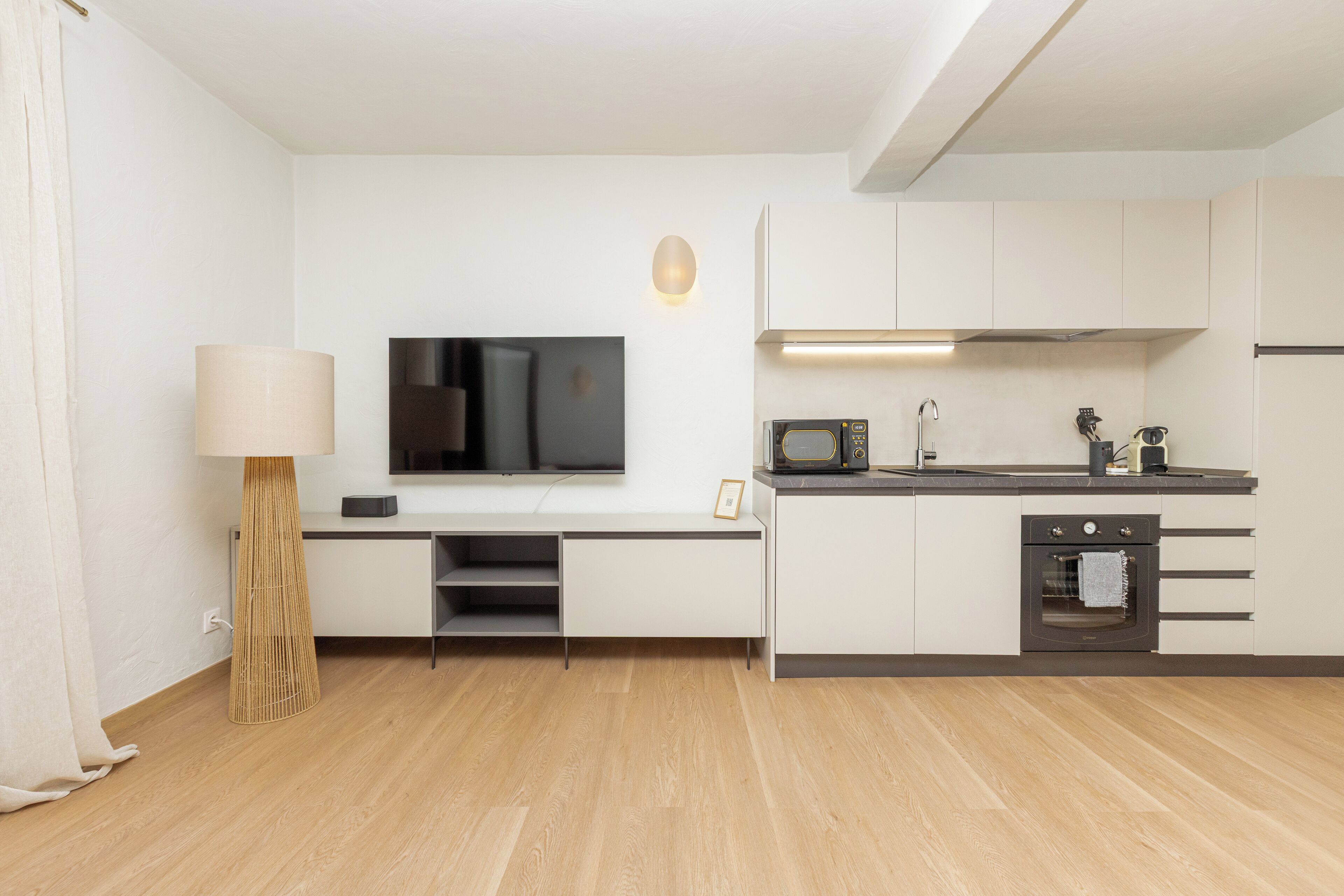 Une cuisine moderne avec des meubles blancs, un four à micro-ondes encastré et un four traditionnel. Un téléviseur à écran plat est fixé au mur au-dessus du plan de travail.