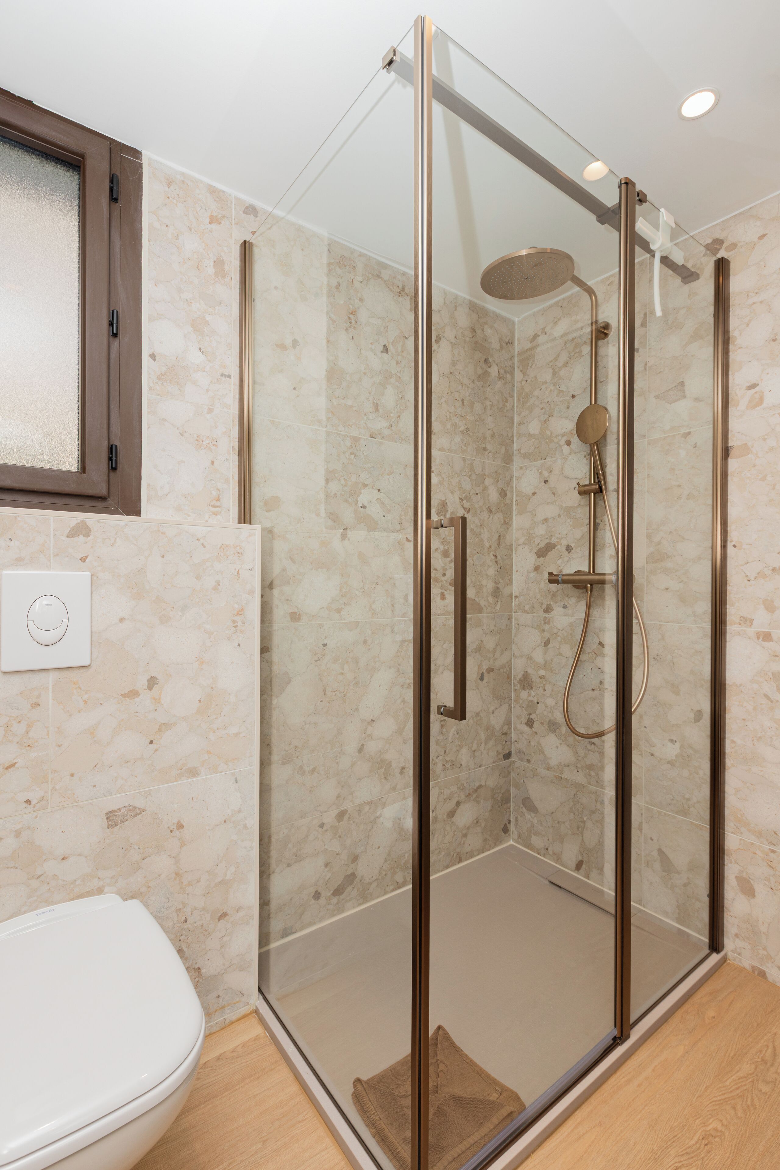 Un baño moderno con cabina de ducha de vidrio, inodoro blanco y pared con azulejos de mármol.
