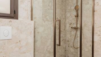 Un baño moderno con cabina de ducha de vidrio, inodoro blanco y pared con azulejos de mármol.