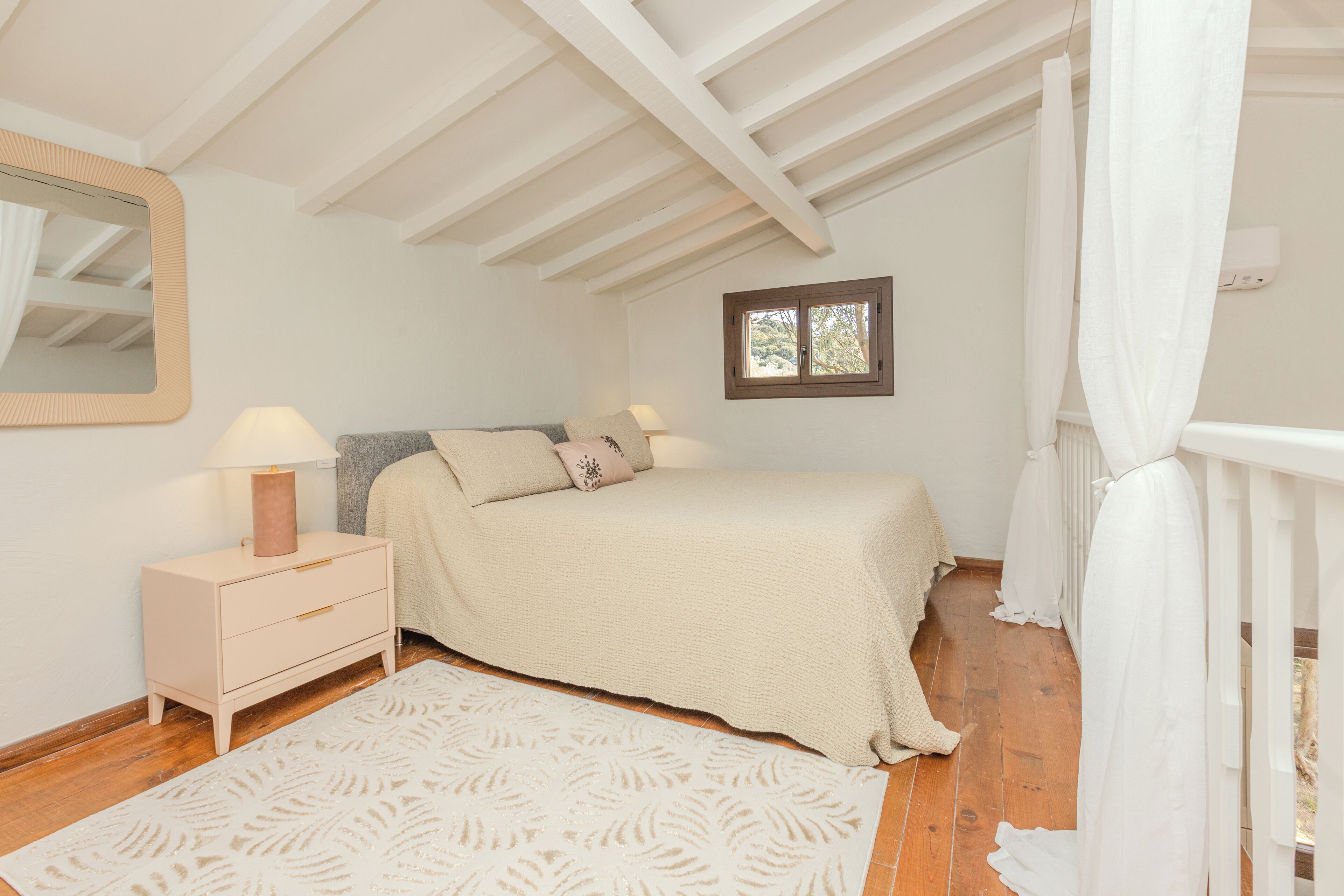 A bedroom with a bed, nightstand, lamp, and a window with curtains.