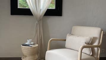 Ein Zimmer mit Fenster, einem Sessel, einem kleinen Tisch mit Tasse und Büchern sowie einem Teppich.