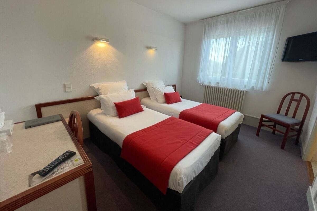 Habitación de hotel con dos camas, un televisor, una silla y una mesa con control remoto.