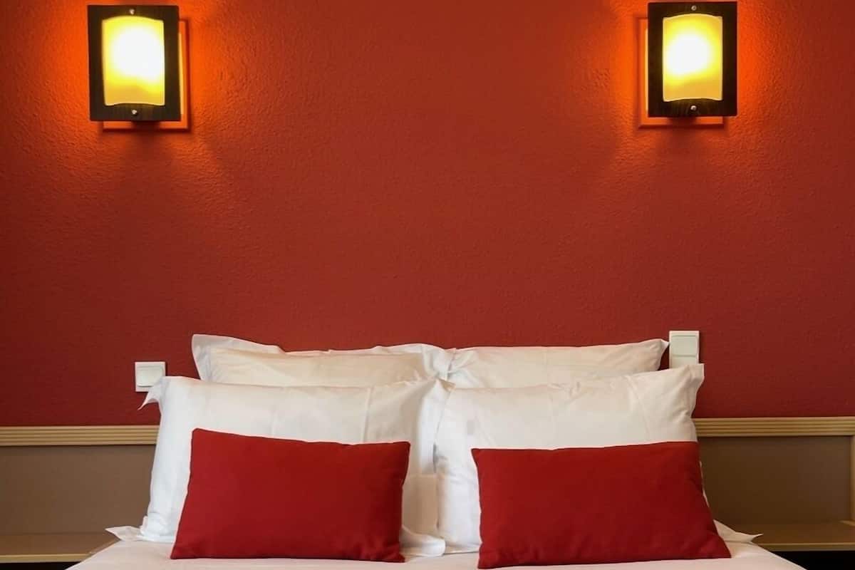 Habitación de hotel con cama, ropa de cama roja y blanca, y dos luces fijadas a la pared.