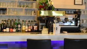 Un espace bar avec un comptoir en bois, des étagères remplies de bouteilles et deux tabourets de bar noirs.