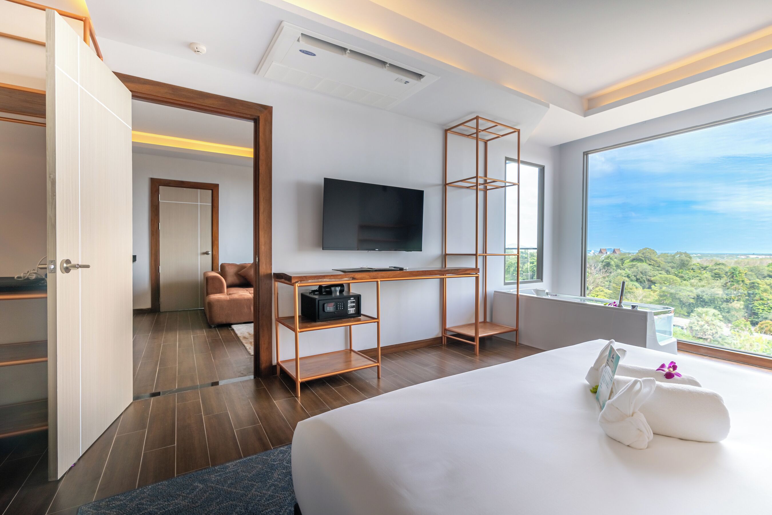 Una habitación de hotel moderna con una cama grande, un televisor, un escritorio de madera y vistas al exterior.