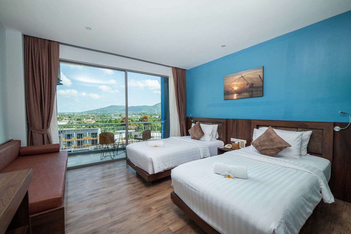 A hotel room with two beds, a balcony, and a view of a cityscape.