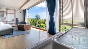 A modern bedroom with a large window, a bathtub, a sofa, and a wooden floor. - The Blue (Chalong)