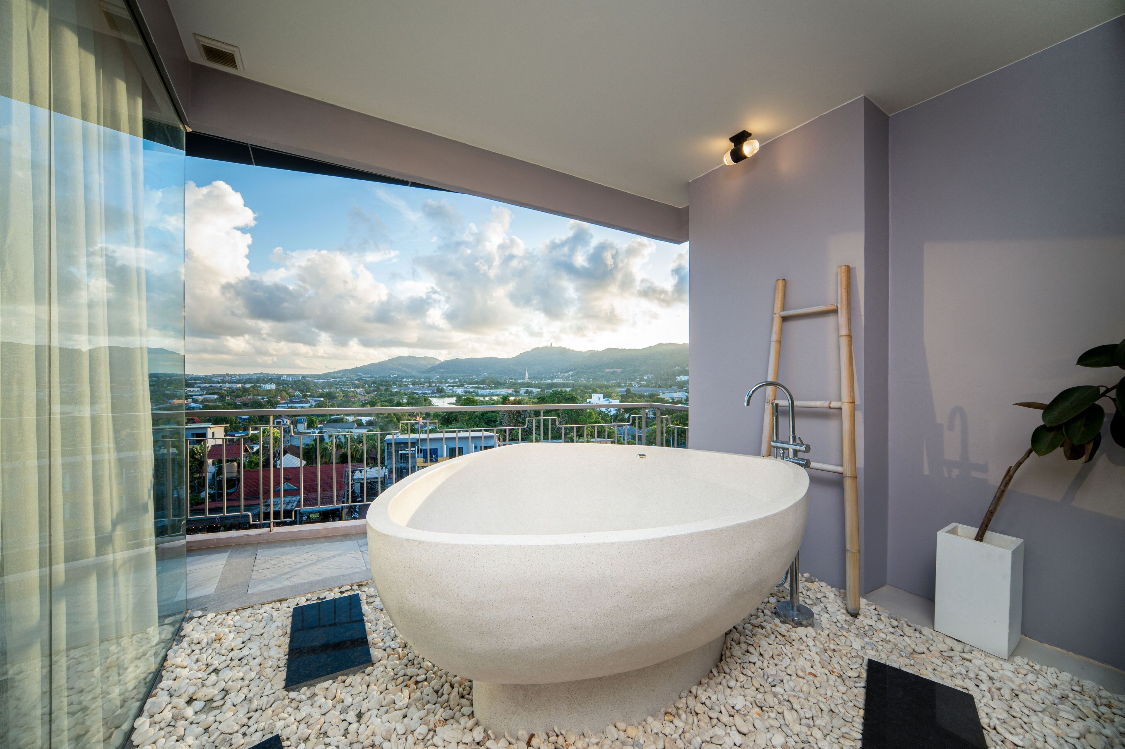 Un baño moderno con una bañera independiente, una escalera de bambú y vistas de la ciudad a través de amplios ventanales.
