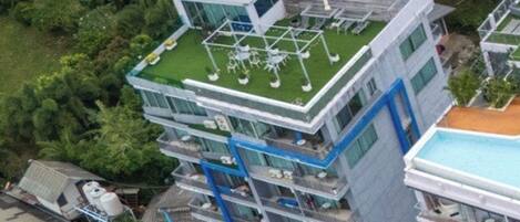 A multi-story building with a rooftop terrace, balconies, and a swimming pool.