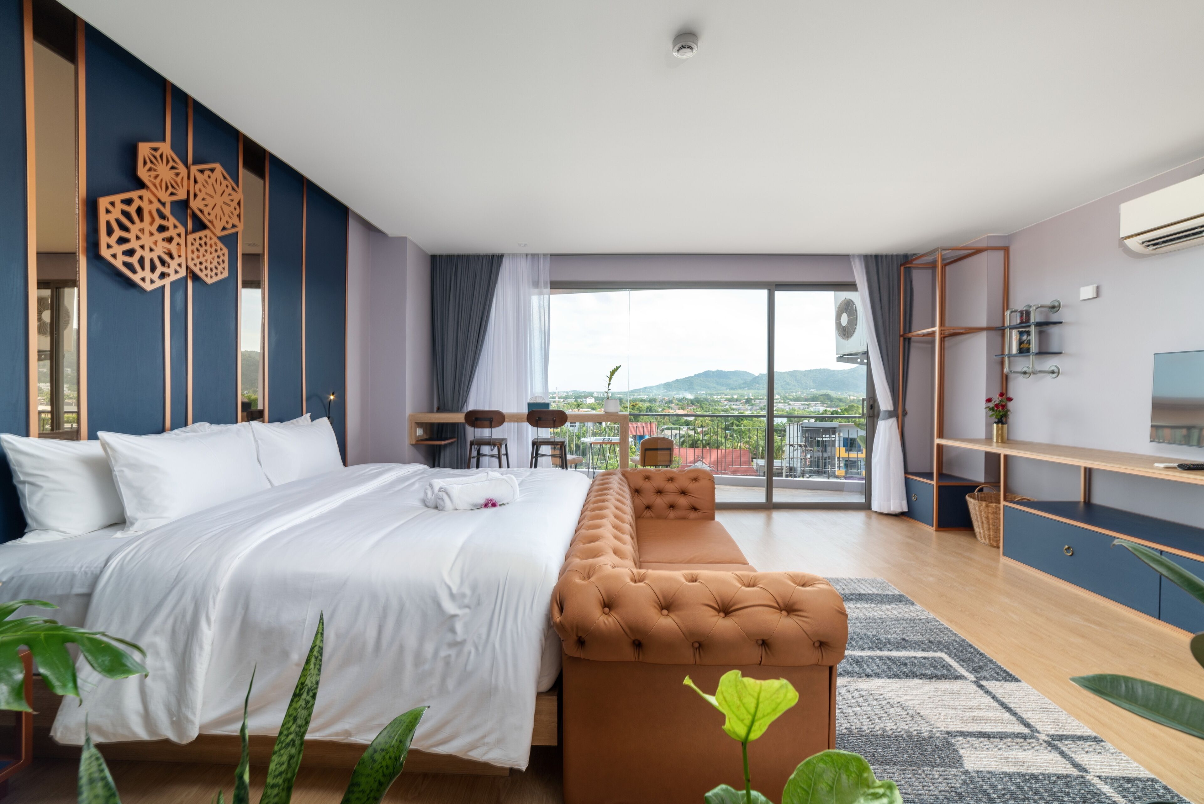 A modern hotel room with a large bed, a sofa, a balcony with a view, and a desk area.