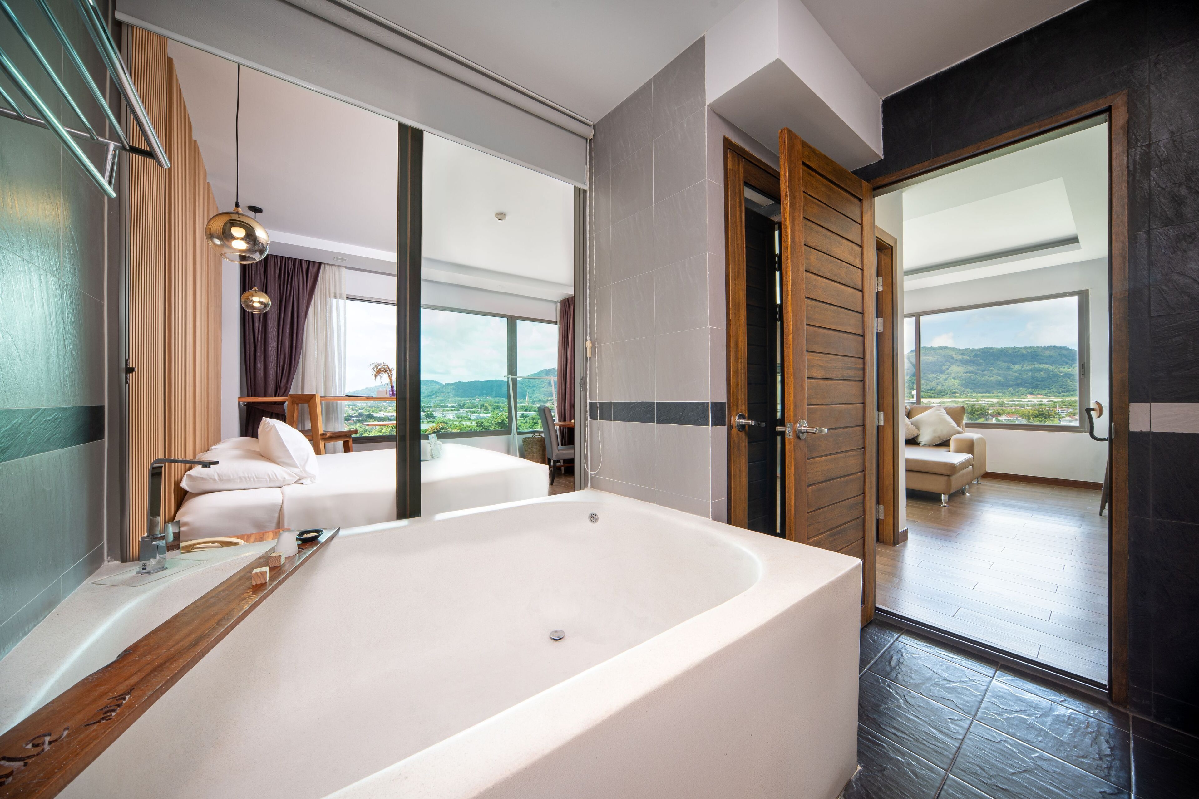 A modern bathroom with a large bathtub, a wooden vanity, and a view of a balcony with a sofa.