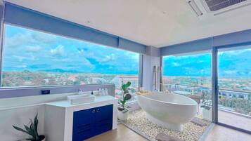 A modern bathroom with a freestanding bathtub, a large window, and a city view.
