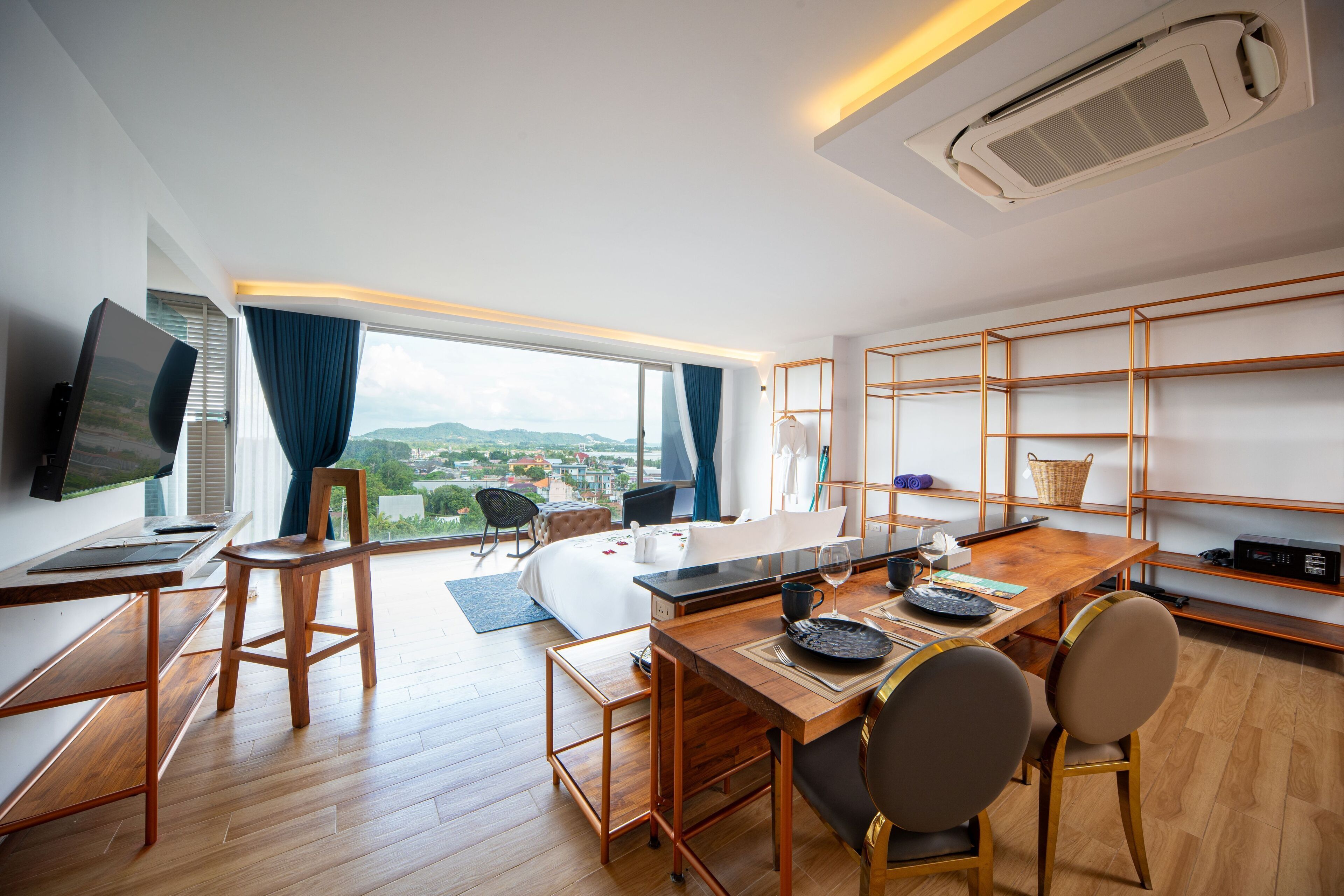 A modern hotel room with a wooden desk, a television, a bed, and a large window offering a city view.