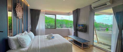 A modern hotel room with a large bed, a TV, and a balcony with a view of greenery.