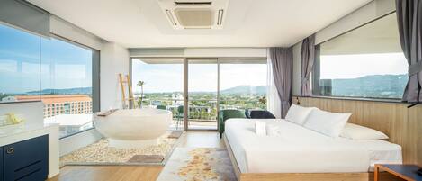 Una habitación de hotel moderna con una cama grande, un área de descanso con una silla, una mesita y vistas a la ciudad a través de amplios ventanales.
