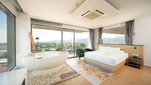 A modern hotel room with a large bathtub, a bed, a view of the city, and a large window. - The Blue (Chalong)