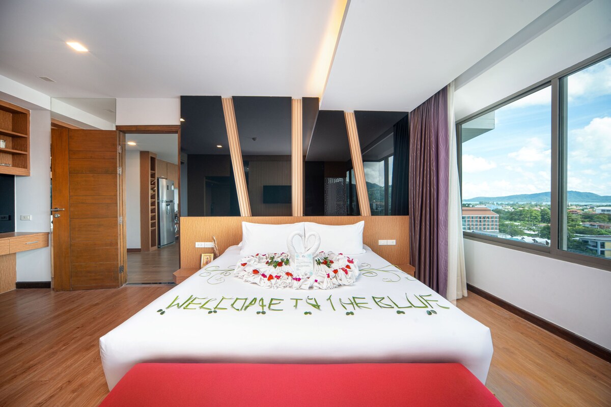 A modern hotel room with a large bed, a view of the city, and a wooden floor.